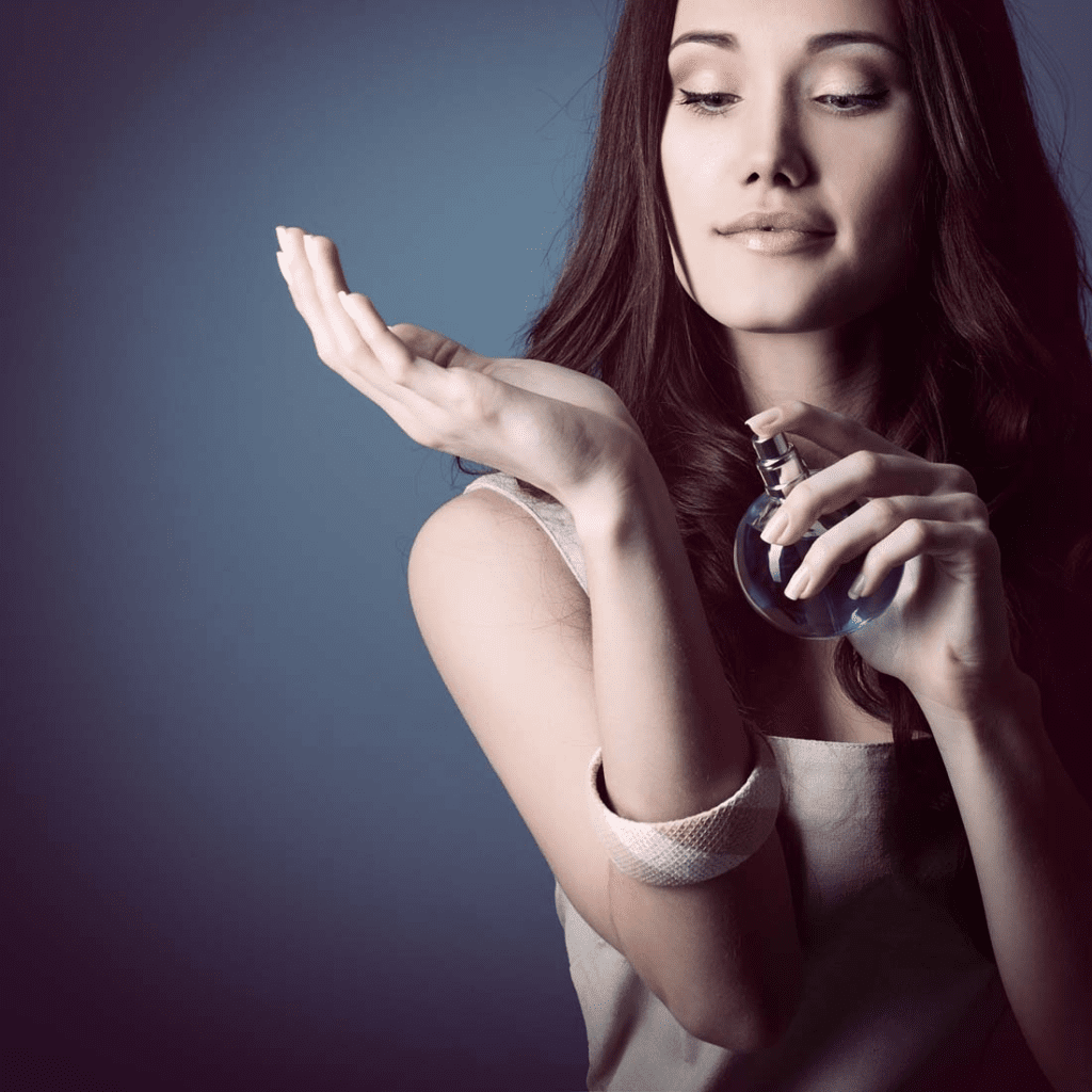 Woman applying perfume from a blue bottle, demonstrating the use of dipropylene glycol in fragrance solvents.