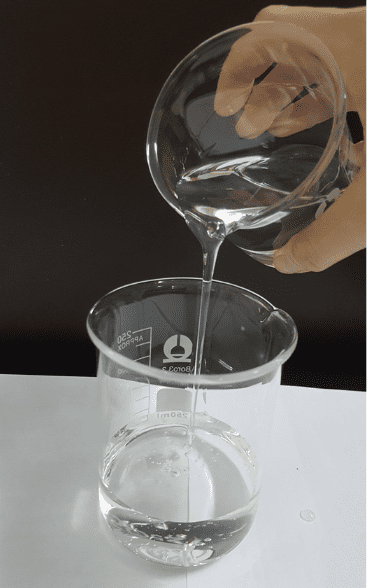 Pouring a clear, viscous liquid from a beaker into a measuring cup.