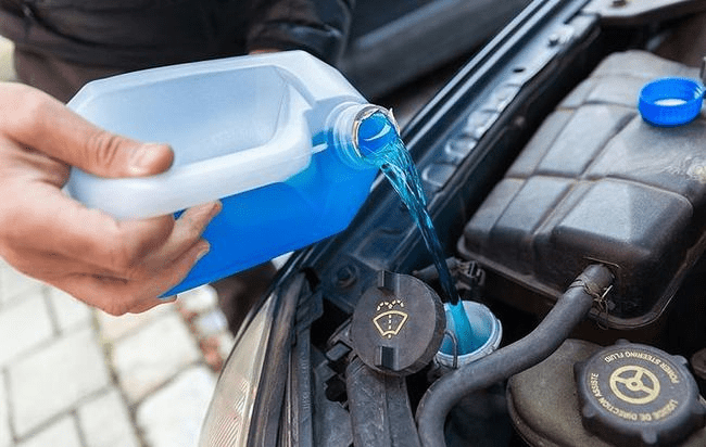 Pouring blue antifreeze into a car's engine coolant reservoir.