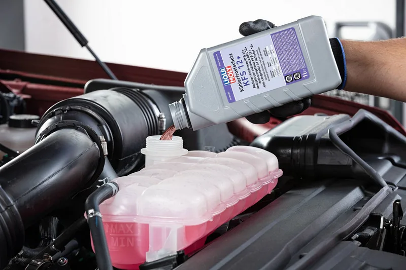 Technician refilling car radiator with propylene glycol antifreeze.