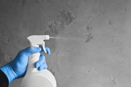 Hand in blue glove spraying liquid from a white disinfectant spray bottle.