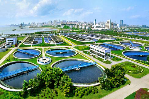 Aerial view of a modern wastewater treatment plant with circular settling tanks and lush greenery, showcasing environmental management.